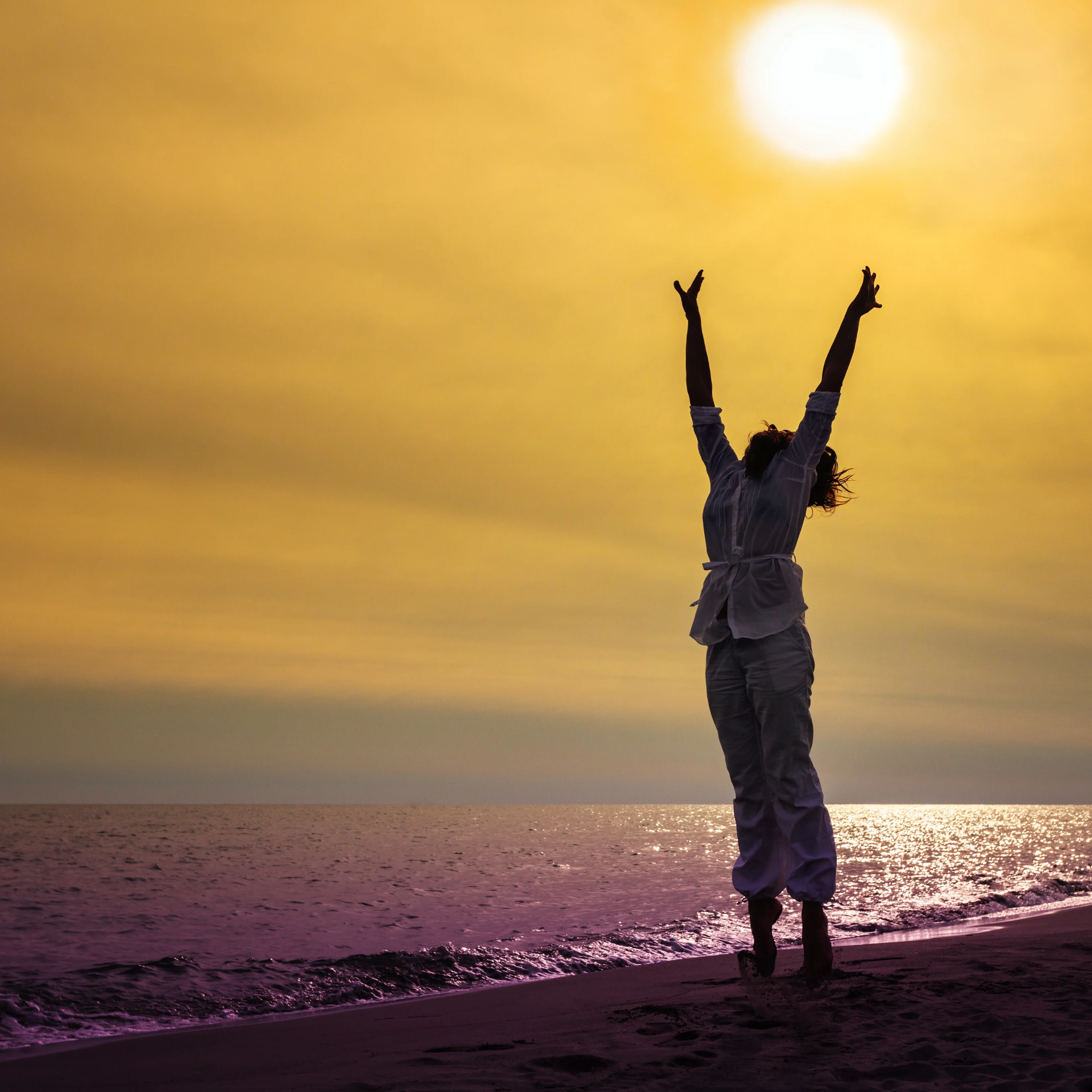 Person with arms raised joyfully on a beach towards the sun during sunset or sunrise